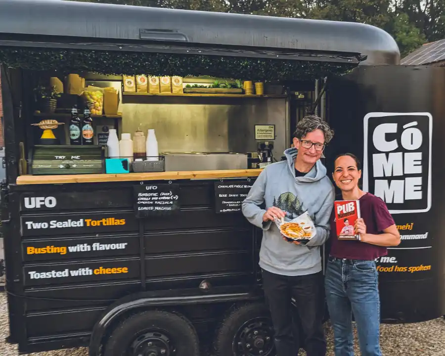 Ari and James Dowdeswell outside the CóMeme trailer at Barsham Brewery, holding The Pub Manifesto and a UFO
